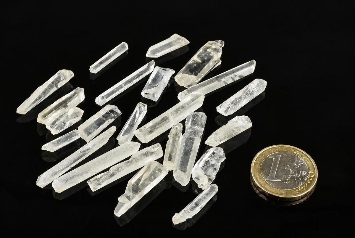 Several clear quartz points on a dark surface, with a one-euro coin for scale.