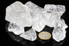 Rough clear and milky-white crystal pieces rest on a glossy black surface beside a coin.