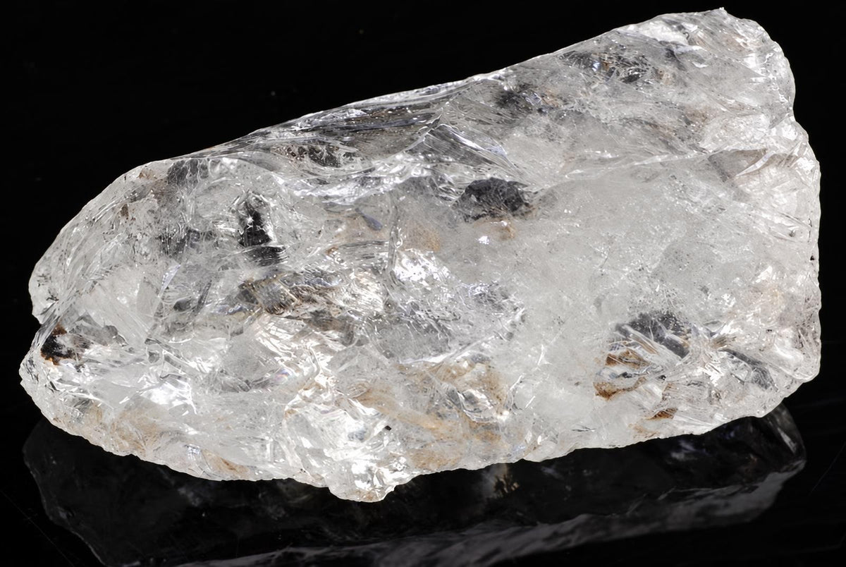 A raw quartz crystal with a clear, glassy appearance and dark inclusions on a black surface.