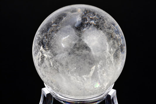 A clear quartz sphere with internal white and dark inclusions rests on a transparent stand against a black background.