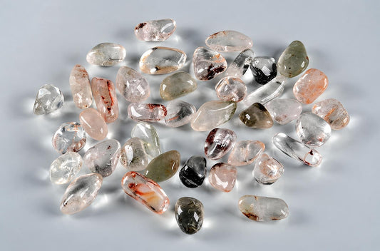 A pile of polished quartz stones with various inclusions, including dark and reddish-brown spots, on a pale surface.