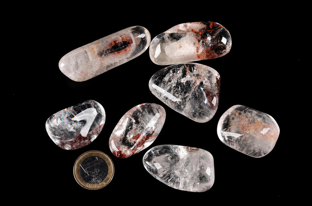 Polished clear stones with cloudy white areas and reddish-brown inclusions lie beside a one-euro coin on a black background.