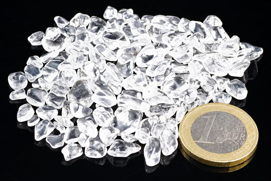 A pile of small, clear quartz stones on a dark surface next to a one euro coin.