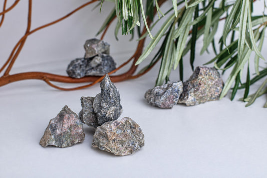 Several rough, multi-colored rocks with grey and pink speckles rest on a pale surface near green leaves.