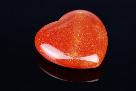 A polished, heart-shaped red aventurine stone with golden flecks rests on a dark surface.