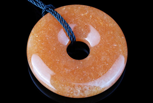 A round, orange-brown pendant with a central hole and pale patches, threaded on a dark blue cord against a black background.