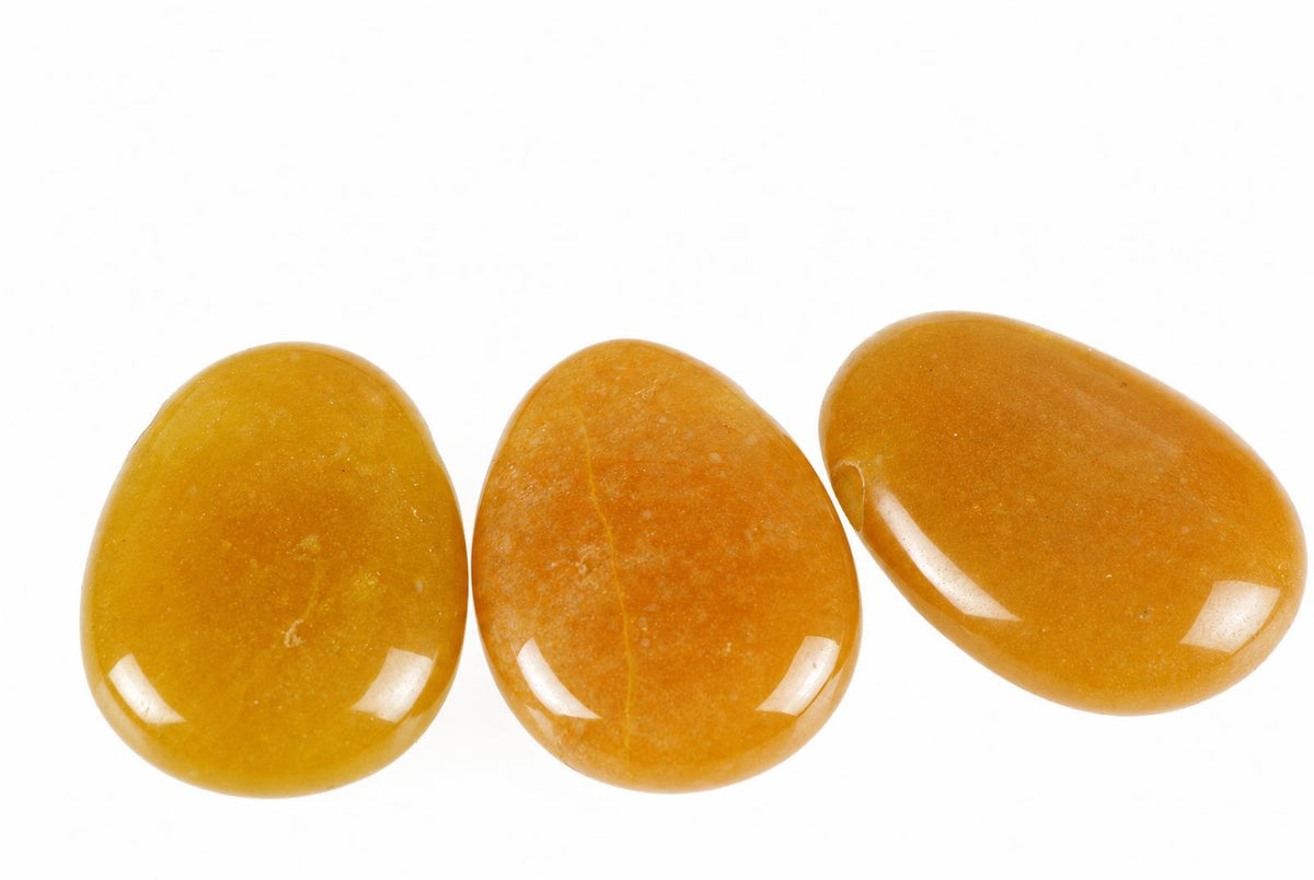 Three smooth, polished stones in shades of yellow and orange arranged on a white surface.