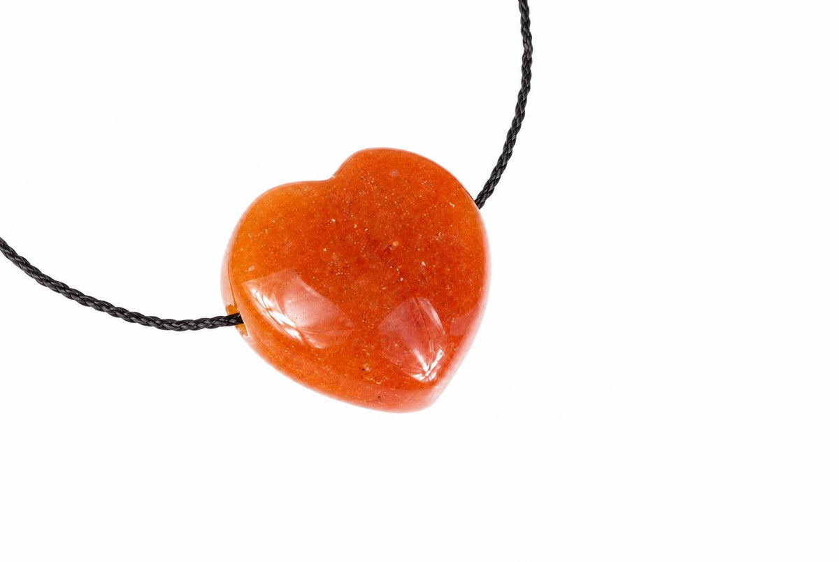 A heart-shaped red aventurine pendant on a dark cord against a white background.