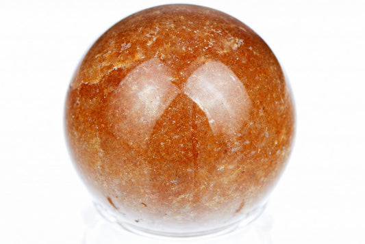 A polished, round sphere with a brownish-orange surface and lighter patches sits on a clear stand against a white background.