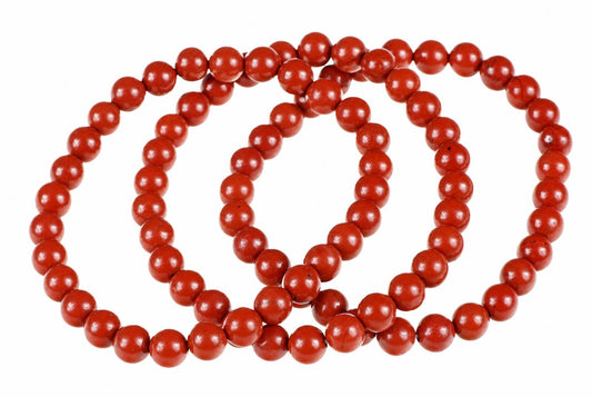 A red jasper bracelet with round beads arranged in a loop on a white surface.