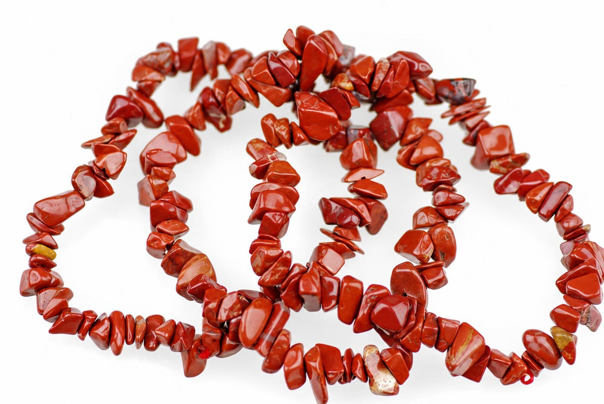 A necklace of irregular red jasper chips arranged in a loose coil on a white surface.