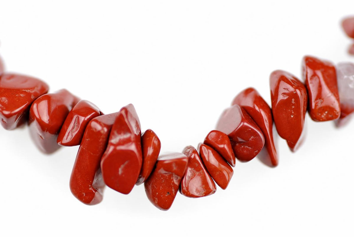 A strand of polished red jasper chips arranged in a loose curve on a white surface.