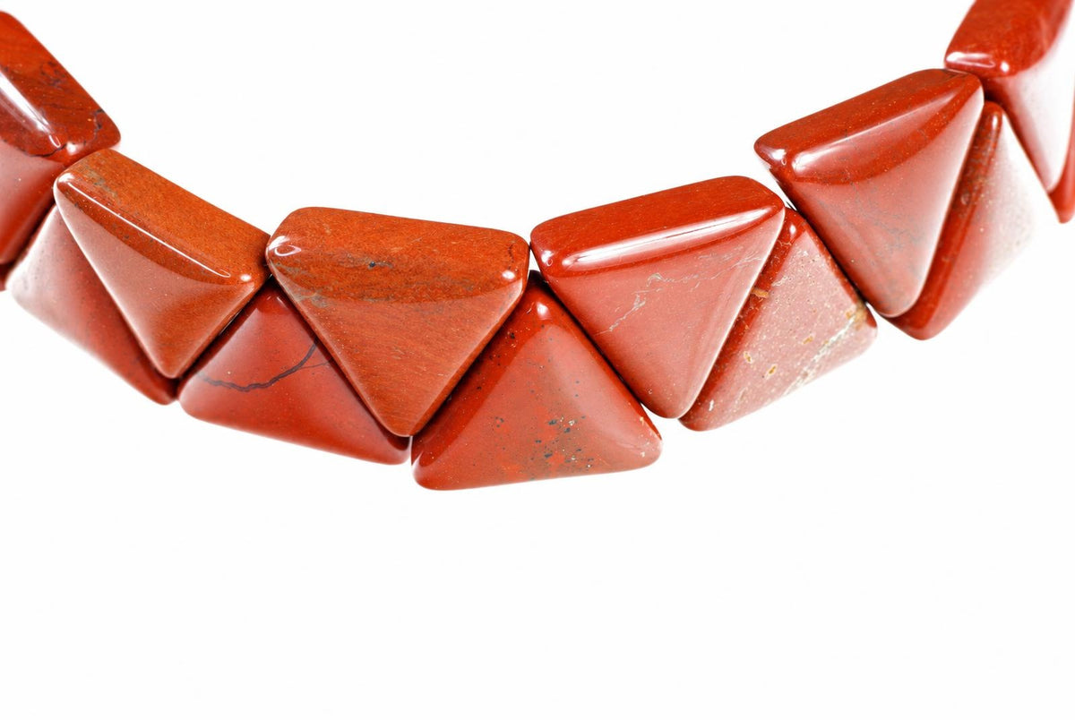 A bracelet with polished, triangular red jasper beads arranged in a curved line against a white background.