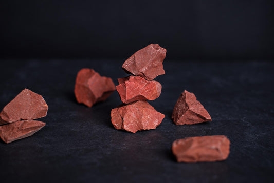 Red jasper India – Raw pieces arranged on a dark surface, some stacked in the center.