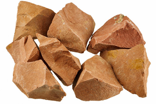A pile of raw red jasper stones with brown and yellow tones on a white background.