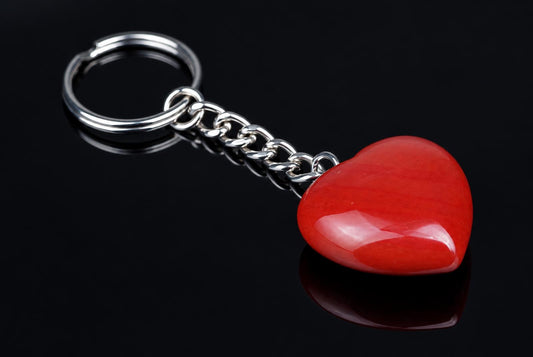 A silver-toned keychain with a polished red heart-shaped pendant on a dark reflective surface.