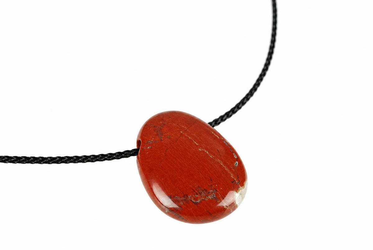 A polished red jasper pendant with dark veins hangs on a black cord against a white background.