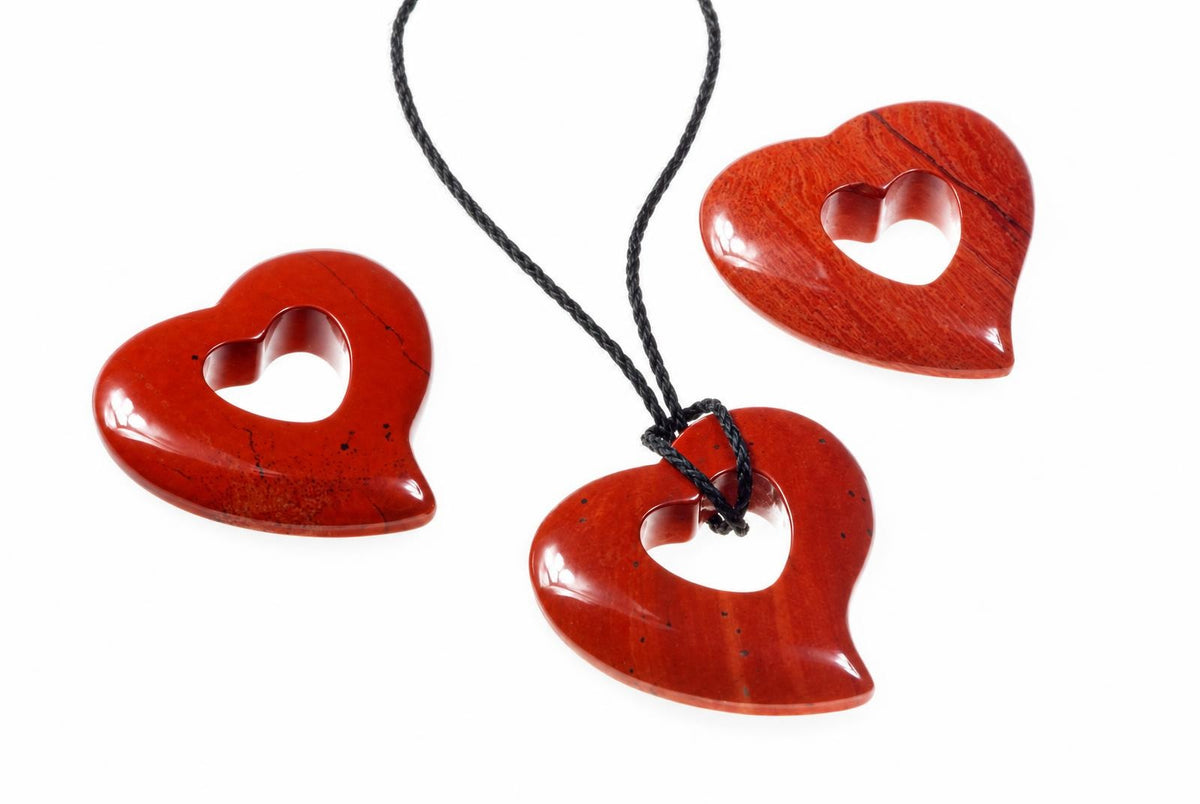 Three red jasper heart pendants with cutouts, one on a black cord, on a white background.