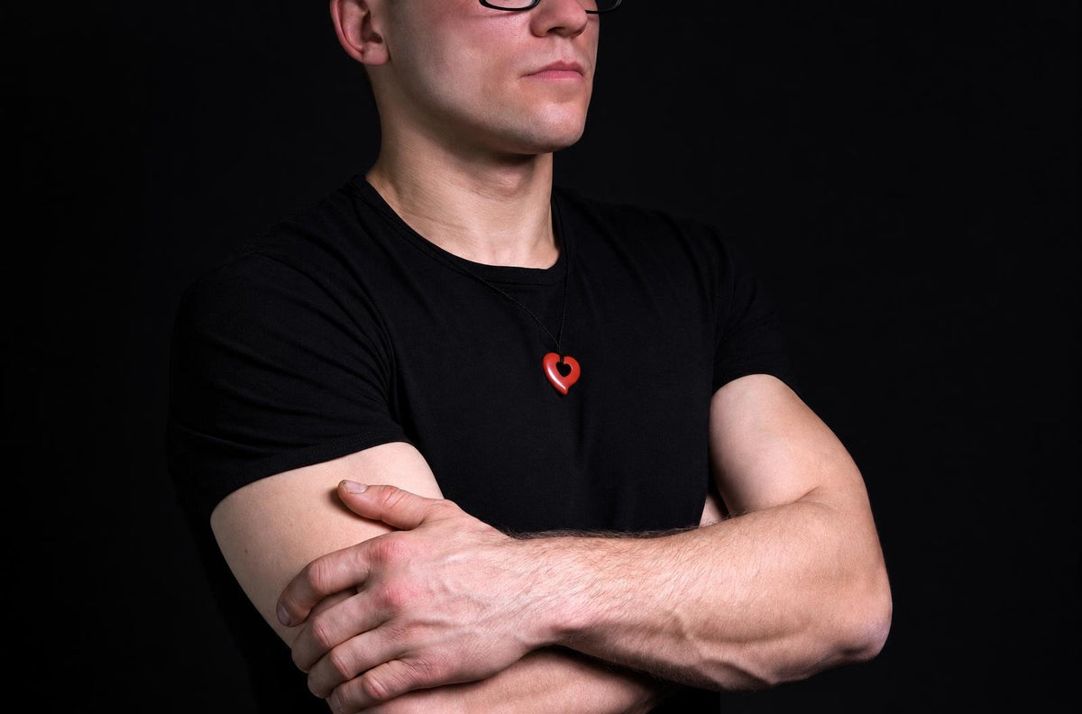 A man wears a black t-shirt with a red heart-shaped pendant on a dark surface.