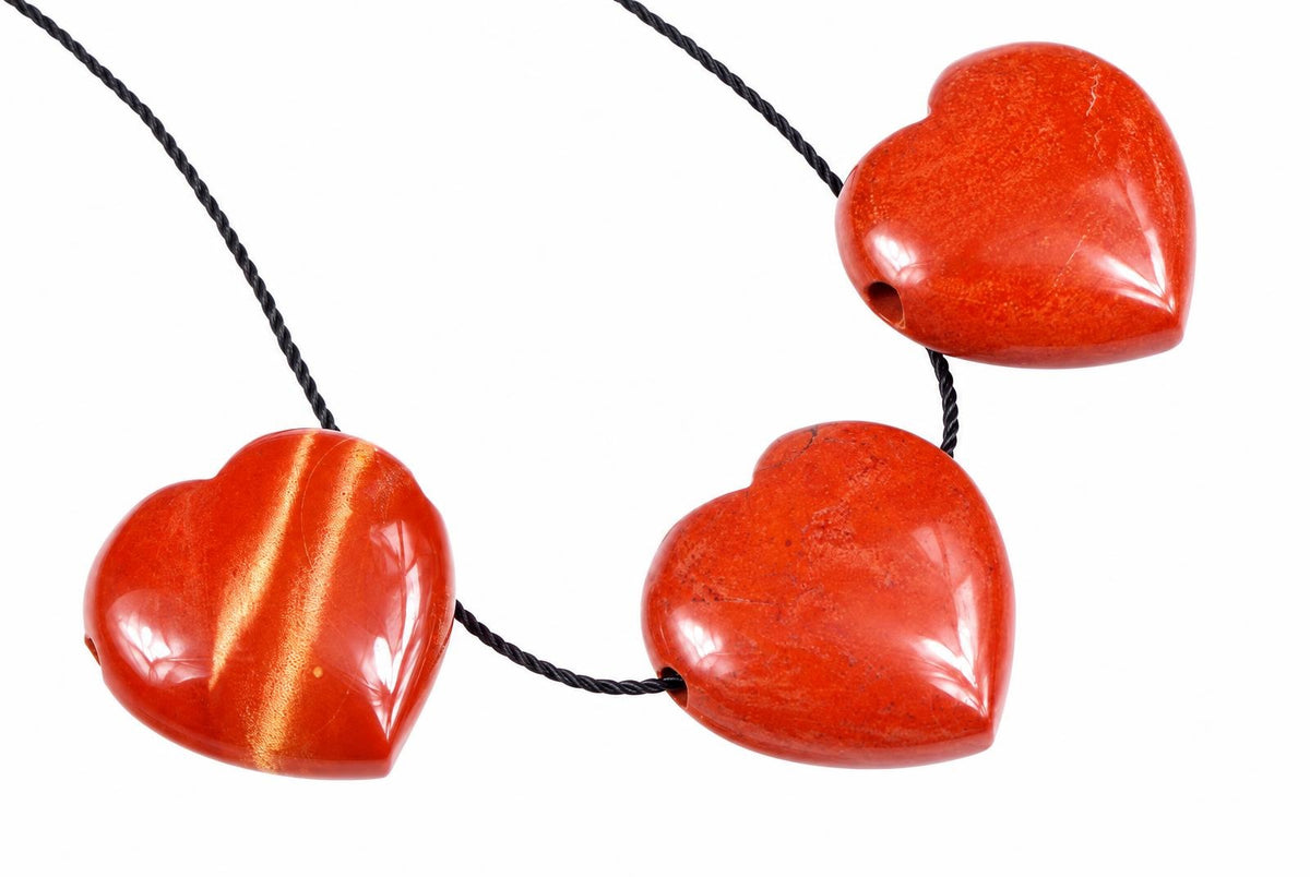 Three polished red heart-shaped beads on a black cord against a white background.