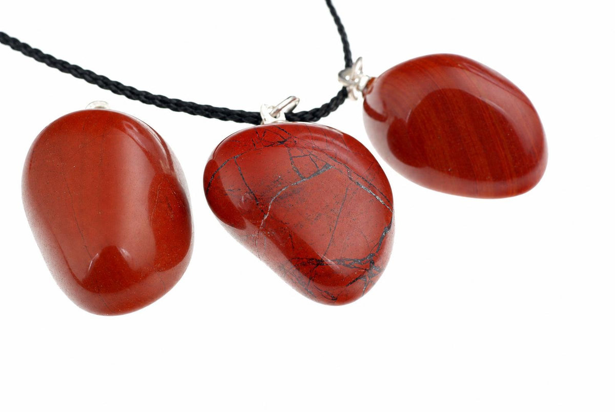Three polished red jasper pendants on a black cord against a white background.