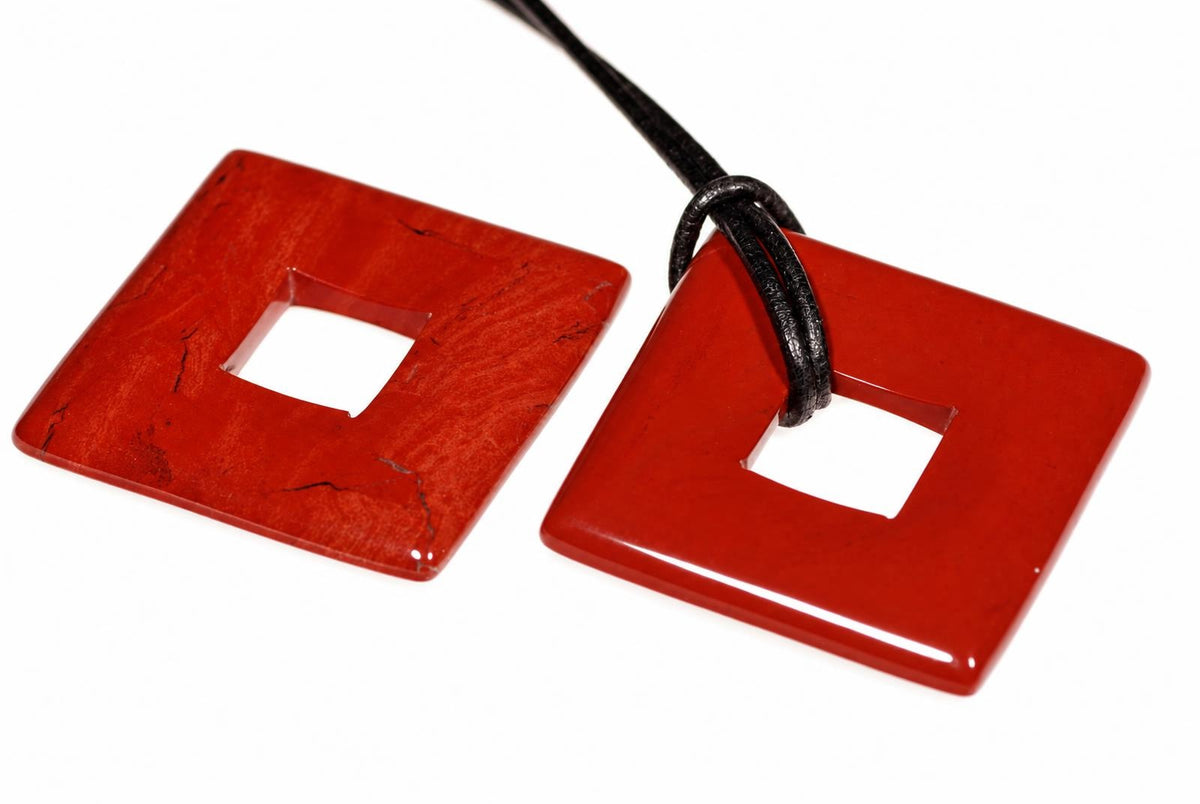 Two red square pendants with central holes; one has a black cord looped through it, both on a white surface.