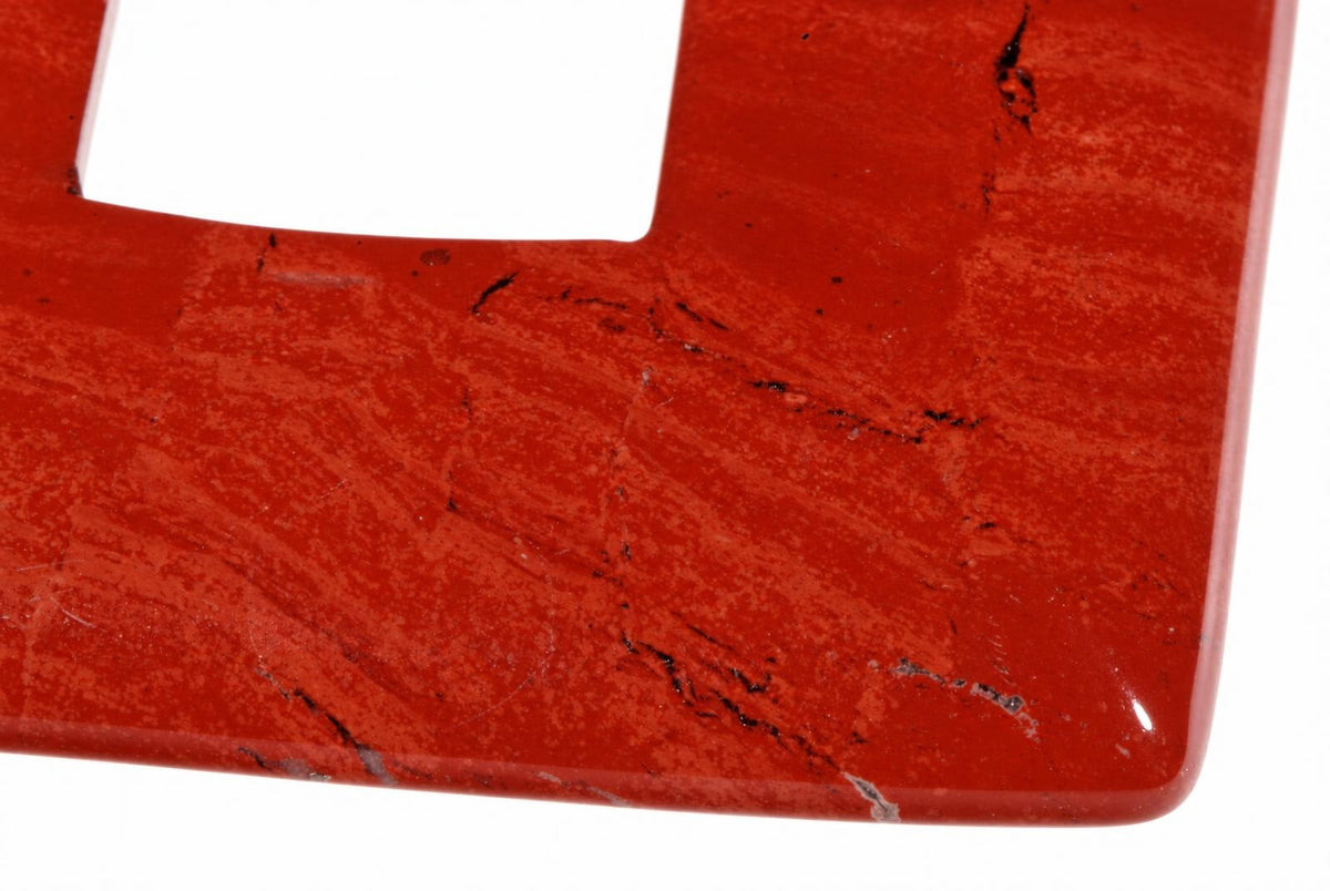 A close-up of a red jasper pendant with black veins and a square cutout, set against a white background.