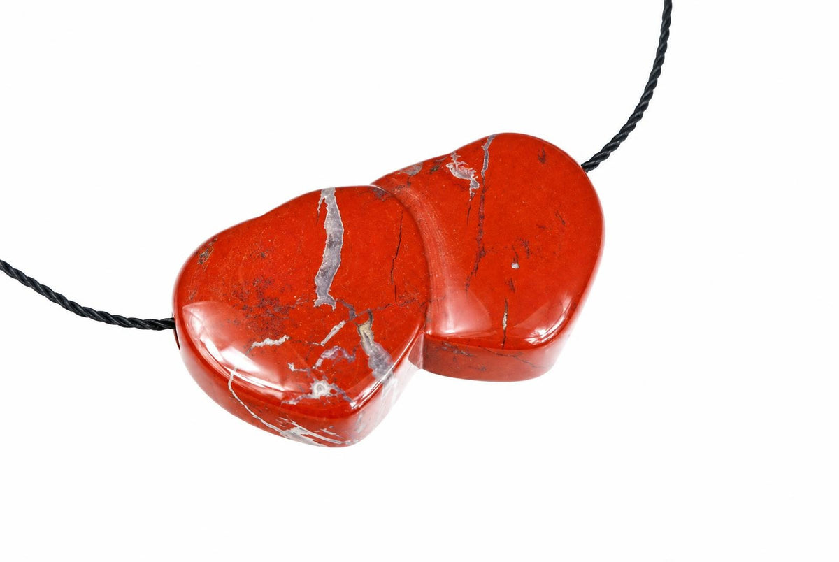 A polished red pendant with white veins, shaped like two joined hearts, on a black cord against a white background.