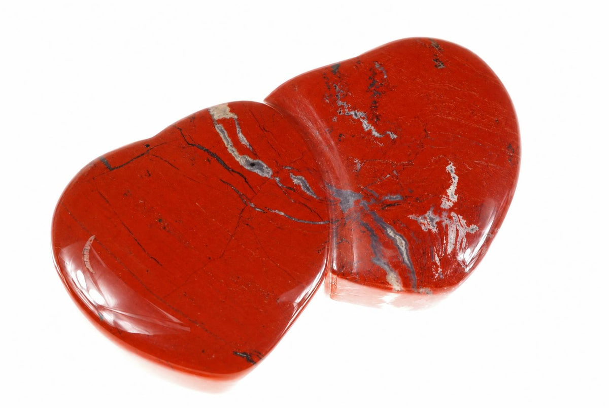 A polished, heart-shaped red stone with dark and silver-toned veins on a white surface.