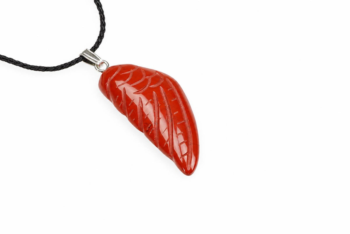 A red jasper wing pendant shows carved feather grooves and pale markings, suspended from a black cord against a white background.