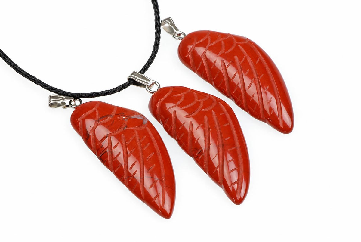 Three red jasper wing pendants show carved feather grooves and pale markings, arranged with a black cord against a white background.