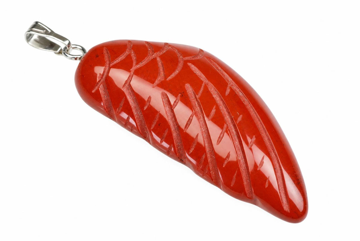 A red jasper pendant shaped like a wing, with carved lines and a silver-toned bail on a white surface.