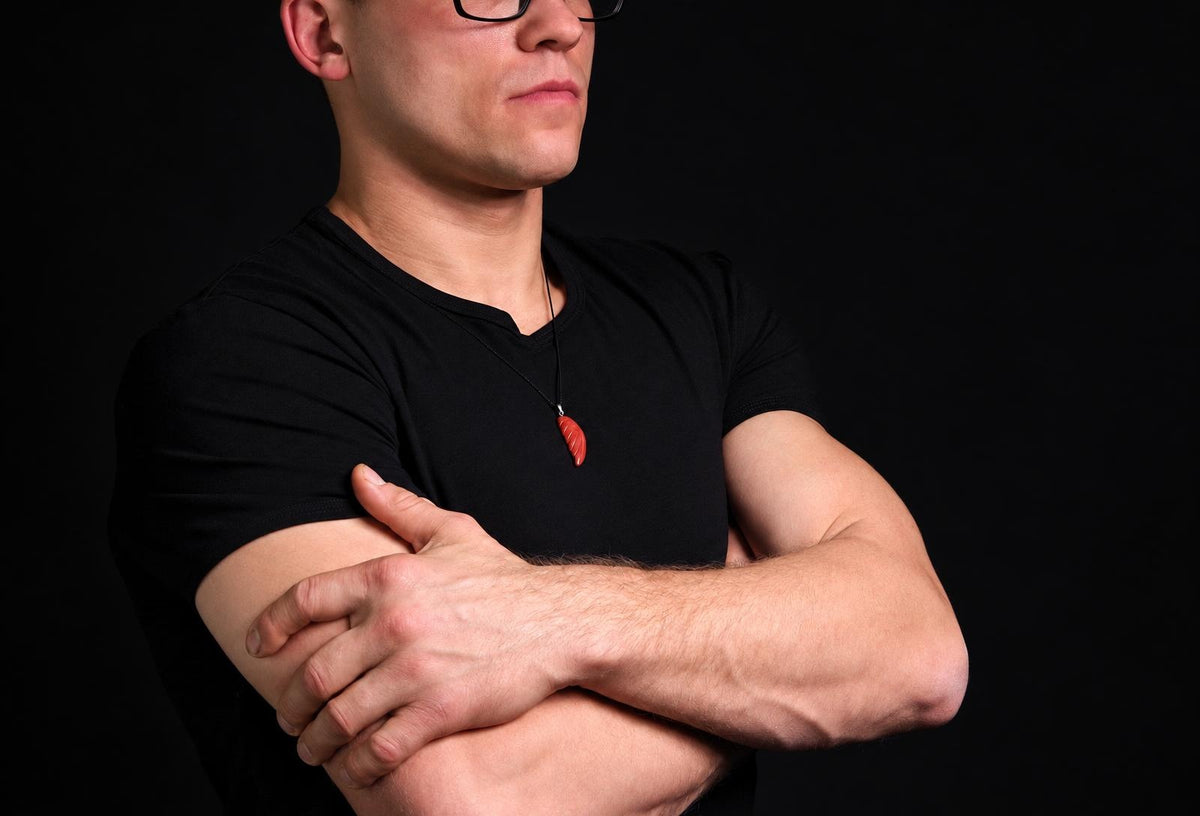 A man in a black t-shirt wears a red pendant shaped like a wing on a dark surface.