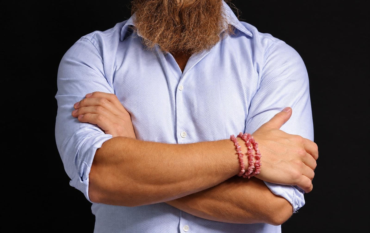 A person with a beard wears three pink chip bracelets on their wrist against a dark background.