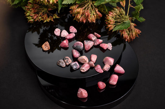 Small polished pink stones with gray and darker patches are scattered over a black circular display among dried flower clusters.