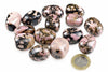 A group of polished rhodonite stones with pink, black and brown patterns on a white surface next to a one euro coin.