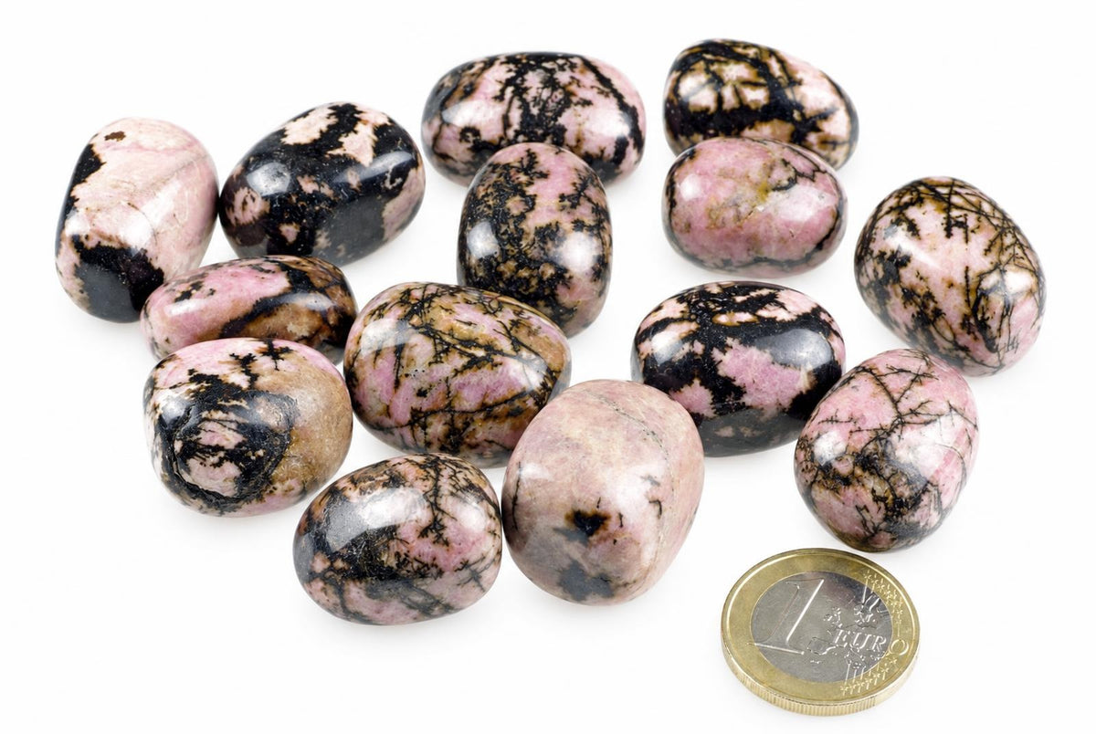 A group of polished rhodonite stones with pink, black and brown patterns on a white surface next to a one euro coin.