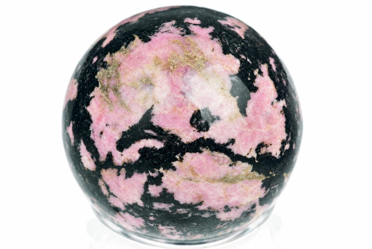 A polished Rhodonite sphere with pink, black and gold-coloured patterns on a white surface.