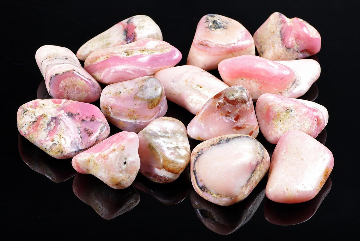 A collection of polished rose opal stones with pink, white and dark inclusions arranged on a dark reflective surface.