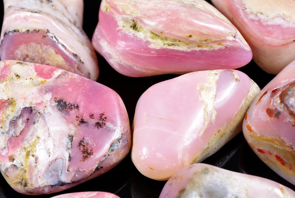 Several polished rose opal stones with pink, white and dark inclusions rest on a dark surface.