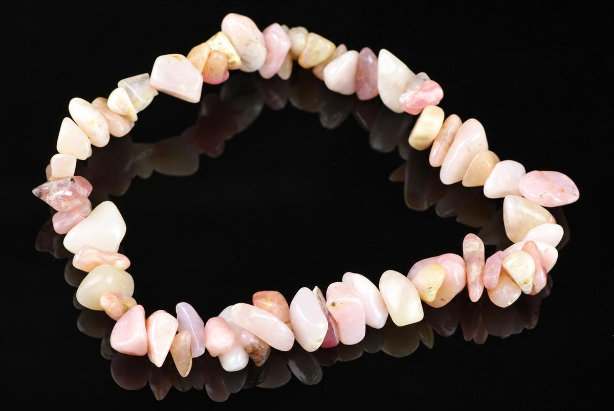 A bracelet made of irregular rose opal chips in pink, cream and pale yellow tones on a dark reflective surface.