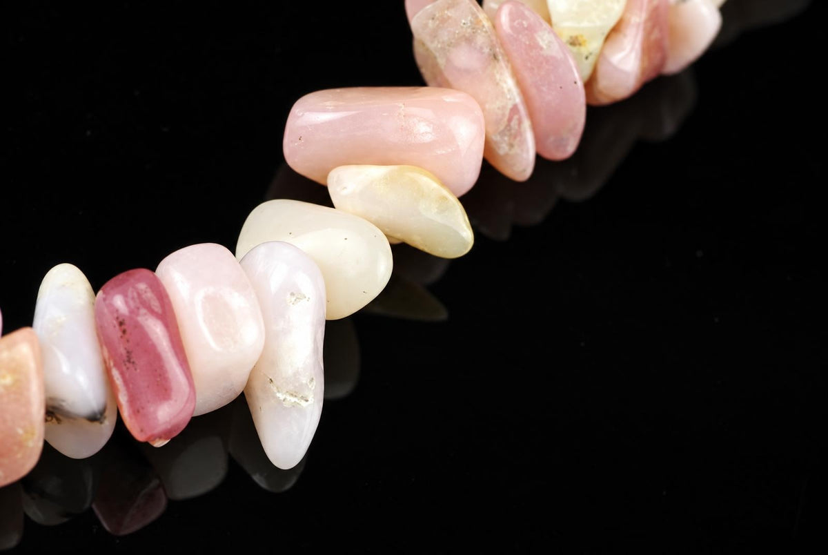 A bracelet of polished, irregular chips in pink, white and cream tones on a dark surface.