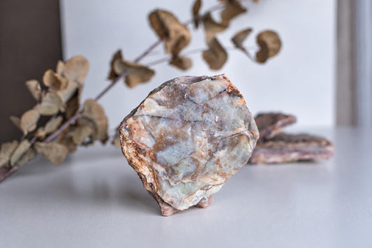 A raw, irregular stone with a polished face showing white, grey and brown patterns stands on a pale surface.