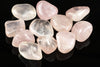 A collection of polished rose quartz stones in pale pink and clear tones, arranged on a dark reflective surface.