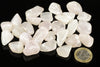 A pile of polished, translucent white to pale pink stones on a dark surface with a one euro coin for scale.