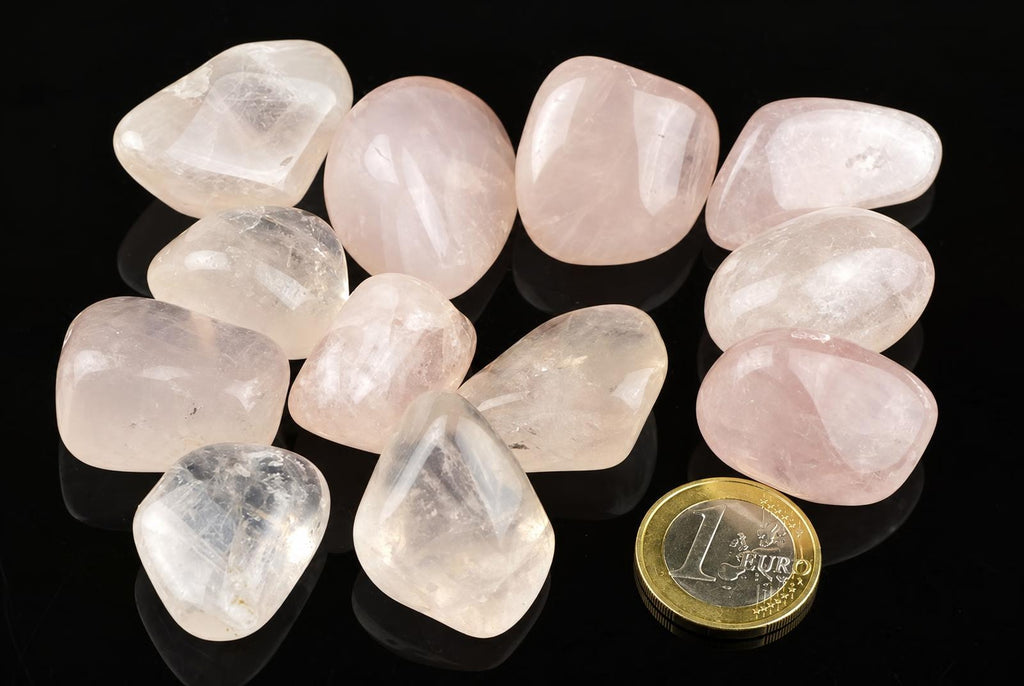A collection of polished rose quartz stones in pale pink and clear tones, arranged on a dark surface with a one-euro coin for scale.