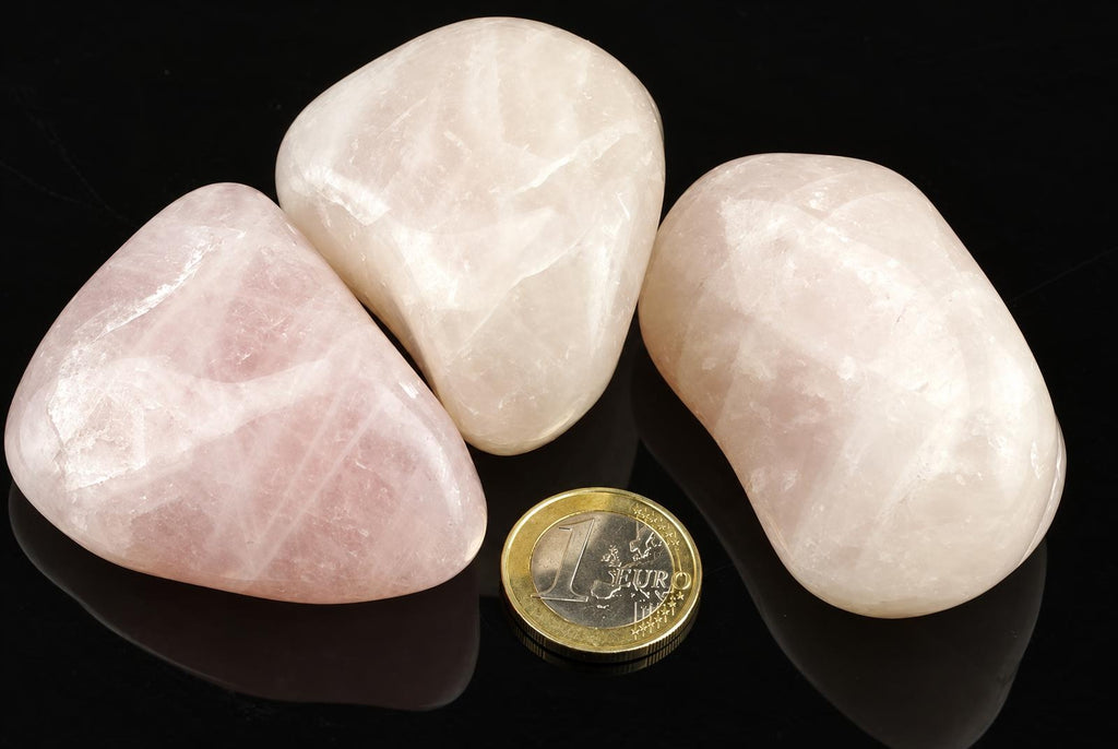 Three polished rose quartz stones on a dark surface with a one euro coin for scale.