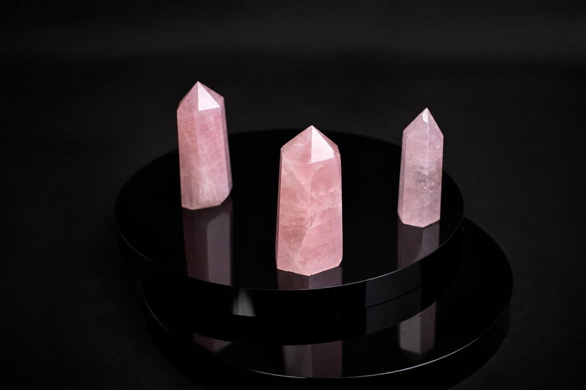 Three pink rose quartz crystal points stand on a glossy black circular base against a dark background.