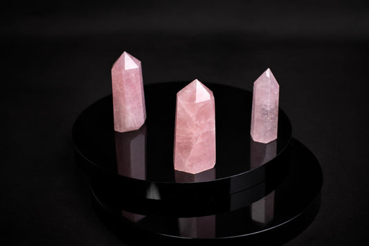 Three pink rose quartz crystal points stand on a glossy black circular base against a dark background.