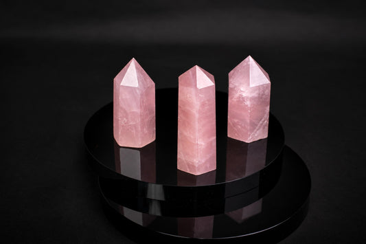 Three pink rose quartz crystal points stand on a dark, reflective circular surface against a black background.